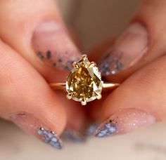 a woman's hand holding a yellow diamond ring with glitters on it and her fingers