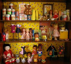 many dolls are sitting on shelves in a room with yellow wallpaper and colorful wall paper