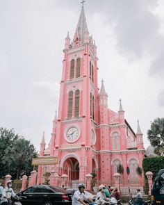 a large pink building with a clock on it's side and people riding motorcycles in front