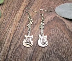 two silver guitar shaped earrings sitting on top of a wooden table