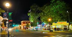 an empty city street at night with people walking on the sidewalk and food carts in the distance