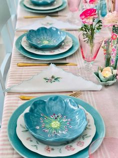 the table is set with blue dishes and pink flowers