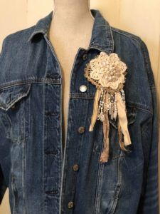 a denim jacket with an applique flower on the front and a ribbon attached to it