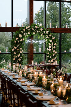 a long table is set with candles and flowers in front of large windows that overlook the trees