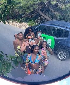 a group of women standing in front of a car taking pictures with their cell phones