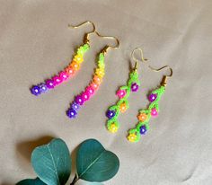 three pairs of beaded earrings sitting next to a plant