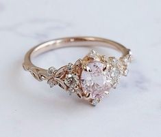 a pink diamond ring with white and yellow diamonds on the side, sitting on a marble surface