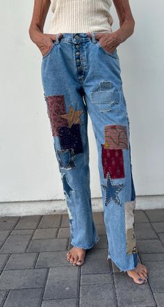 a woman standing in front of a white wall wearing blue jeans with patches on them