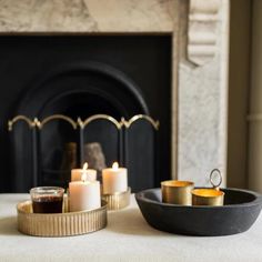 candles are sitting on a table in front of a fireplace with a black bowl next to it