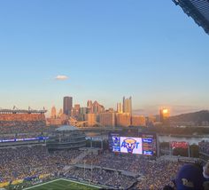 a stadium filled with lots of people watching a football game in the sun set over a city