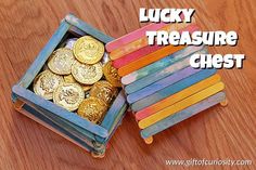 a wooden box filled with lots of gold coins on top of a wooden table next to a pile of sticks