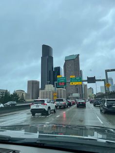 cars are driving down the highway in front of tall buildings and skyscrapers on a cloudy day