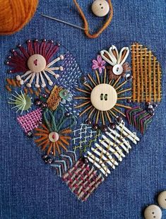 a heart made out of buttons and pins on a piece of blue fabric with two balls of yarn in the background