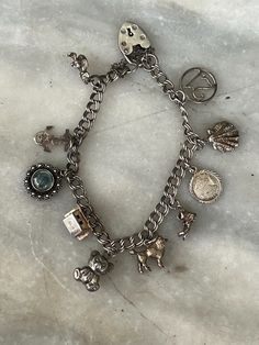 Vintage British silver charm bracelet. Made in the UK between the late 1950s  and early 1970s. The bracelet is fairly light, as are the charms,  making it suitable for a girl to wear. It has 10 charms: '21', shell, Pisces medallion,  boot, poodle, teddy bear, Swiss chalet, evil  eye, anchor, Cornish pinkie. The bracelet is 0.6 cm wide, and 18.5 cm long. The clasp is a heart-shaped 'gate clasp', with  safety chain. Condition is excellent, used. Vintage Dangle Charm Bracelet With Lobster Clasp, Silver Bracelets With Logo Charm For Gift, Silver Bracelets With Logo Charm As Gift, Silver Engraved Metal Charm Bracelet, Engraved Silver Metal Charm Bracelet, Silver Charm Bracelet With Logo For Gift, Silver Charm Bracelet With Logo As Gift, Collectible Vintage Charm Metal Bracelet, Vintage Dangle Charms Bracelets