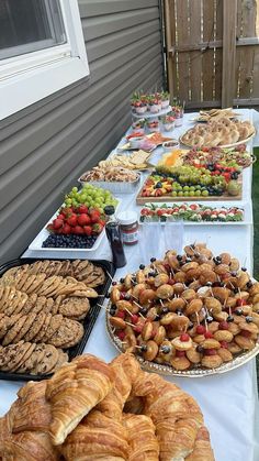 an assortment of pastries and desserts on a long table with white clothed cloth