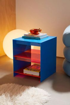 a blue side table with books and a bowl on top, next to a white rug