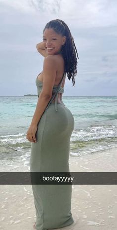 a woman standing on top of a sandy beach next to the ocean wearing a green dress