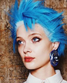 a woman with bright blue hair and piercings on her ears is looking at the camera