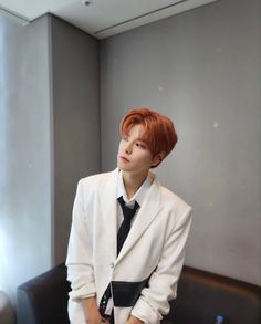 a young man in a white suit and black tie sitting on a brown leather couch