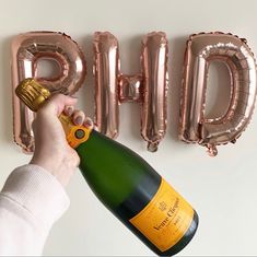 a person holding a bottle of champagne in front of balloons that spell out the word phq