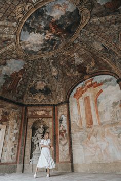 a woman in a white dress standing under a painted ceiling