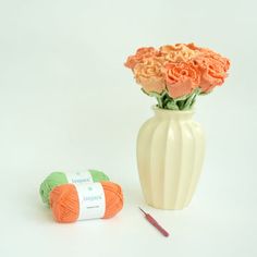 a white vase filled with orange flowers next to a crochet hook and ball of yarn