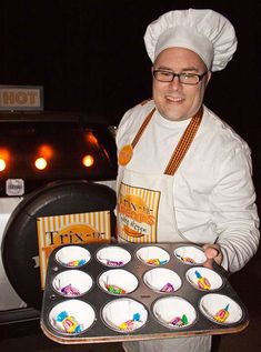 two men in chef's hats holding trays of cupcakes and muffin tins