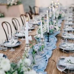 a long table is set with white and blue flowers, candles, and napkins