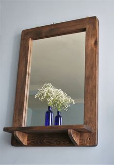 two blue vases sitting on top of a wooden shelf next to a mirror with flowers in it