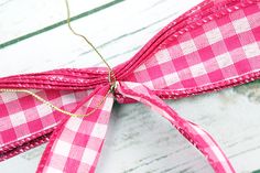 a pink and white checkered ribbon tied to a piece of wood with gold thread