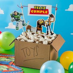 a cardboard box filled with lots of toys and balloons in front of a blue wall