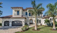 a large house with palm trees in the front yard and two garages on each side