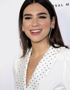 a close up of a person wearing a white shirt and earrings smiling at the camera