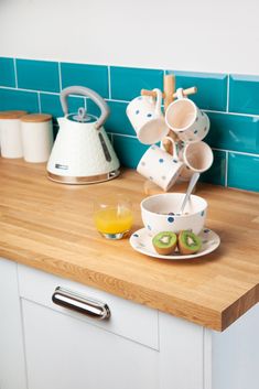 a kitchen counter with cups and tea kettles on it, next to an orange juicer