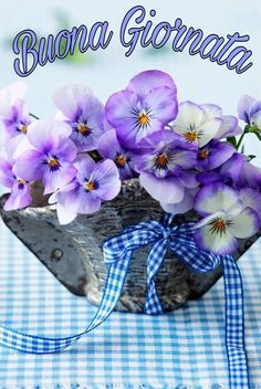 purple flowers are in a wooden bowl on a blue and white checkered tablecloth