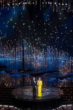 two people standing on stage in front of an audience at a television awards ceremony, with lights behind them