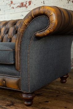 a brown leather couch sitting on top of a wooden floor next to a brick wall