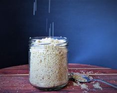 a jar filled with food sitting on top of a wooden table next to a spoon