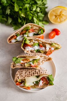 a plate topped with three wraps filled with veggies next to lemon wedges