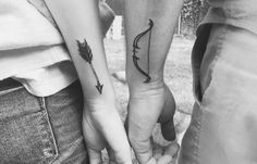 two people holding hands with tattoos on their arms, one has an arrow and the other has