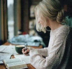 a woman sitting at a table with a book and pen in her hand while writing