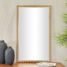 a mirror sitting on top of a wooden table next to two vases and a plant