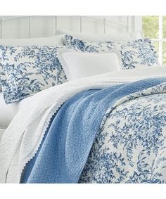 a bed with blue and white comforters on top of it in a bedroom next to a window