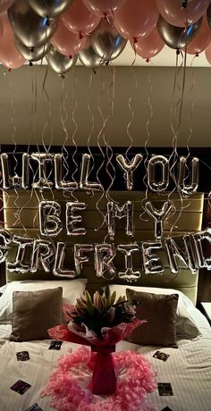 a bed topped with lots of balloons next to a sign that says, will you be my girlfriend?