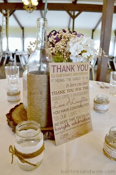 a table topped with jars filled with sand and flowers next to a thank you note