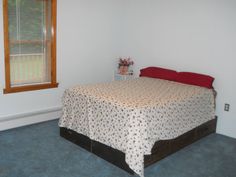 a bed sitting in a bedroom next to a window with blinds on the windowsill