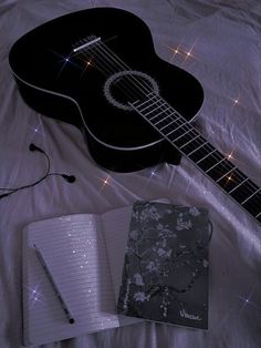 an acoustic guitar, notebook and pen on a bed