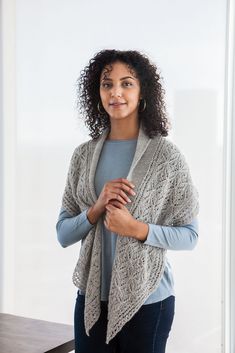 a woman standing in front of a table wearing a gray sweater and blue jeans with her arms crossed