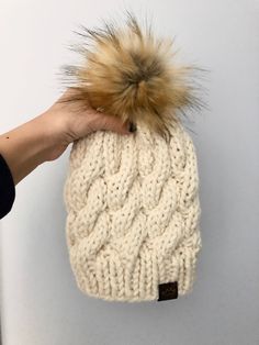 a hand holding a white knitted beanie with a brown pom - pom