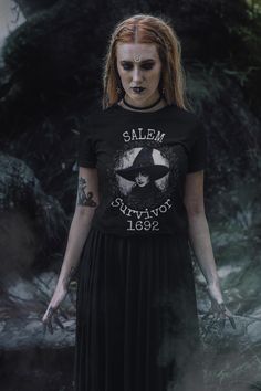 Step back into history with this 'Salem Survivor 1692' t-shirt, a bold tribute to the infamous Salem witch trials. Featuring a striking gothic design with a witch illustration, this shirt captures the essence of resilience and the dark allure of witchcraft. Perfect for Halloween or any time of the year, this unique piece is great for those who embrace the witchy aesthetic and love a bit of historical edge. Whether you're a history buff, a lover of dark fashion, or simply drawn to the witchy vibe, this shirt makes a powerful statement. Ideal for Halloween events, spooky gatherings, or as a standout piece in your everyday wardrobe. Product features - Made from 100% ring-spun cotton for a lightweight and comfortable feel - Classic fit with crew neckline for versatile style - Ethically grown a Gothic Short Sleeve T-shirt For Halloween, Horror Themed Letter Print Crew Neck T-shirt, Horror Style Letter Print Short Sleeve T-shirt, Horror Letter Print Short Sleeve T-shirt, Gothic T-shirt With Letter Print And Short Sleeves, Horror Cotton T-shirt With Letter Print, Horror Themed Letter Print Cotton T-shirt, Gothic Short Sleeve Halloween T-shirt, Witchy Short Sleeve T-shirt With Graphic Print